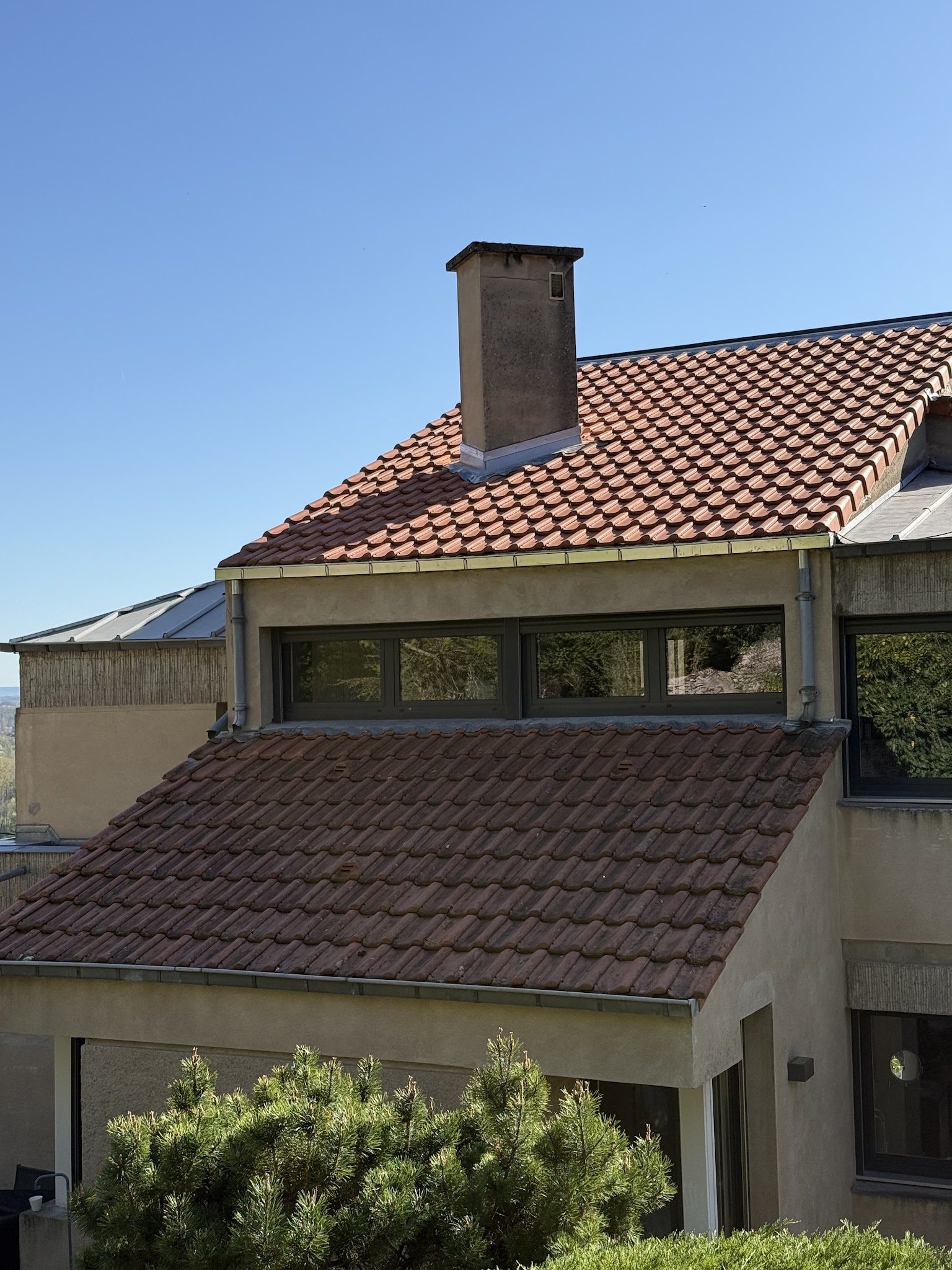 Toiture en tuiles neuves avec cheminée et solin en zinc, sous un ciel bleu
